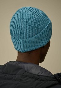 Beanie lavorato a maglia in azzurro chiaro, con texture a coste e una vestibilità aderente. L'immagine mostra la parte posteriore, evidenziando il tessuto morbido e la forma arrotondata.
