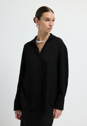 Chemise noire à manches longues avec un motif léopard discret, en tissu doux, dotée d'un col classique et d'une coupe décontractée.