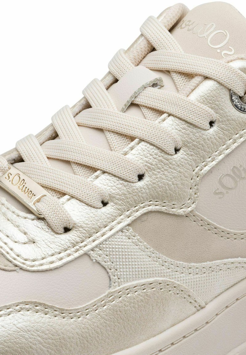 Beige Sneaker aus einer Mischung aus glattem Leder und strukturiertem Stoff, mit metallischen Akzenten, flachen Schnürsenkeln und einem gestickten Designmuster.