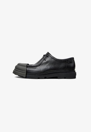 Scarpa in pelle nera con una distintiva punta arrotondata, superficie texturizzata, design con lacci e suola in gomma spessa.