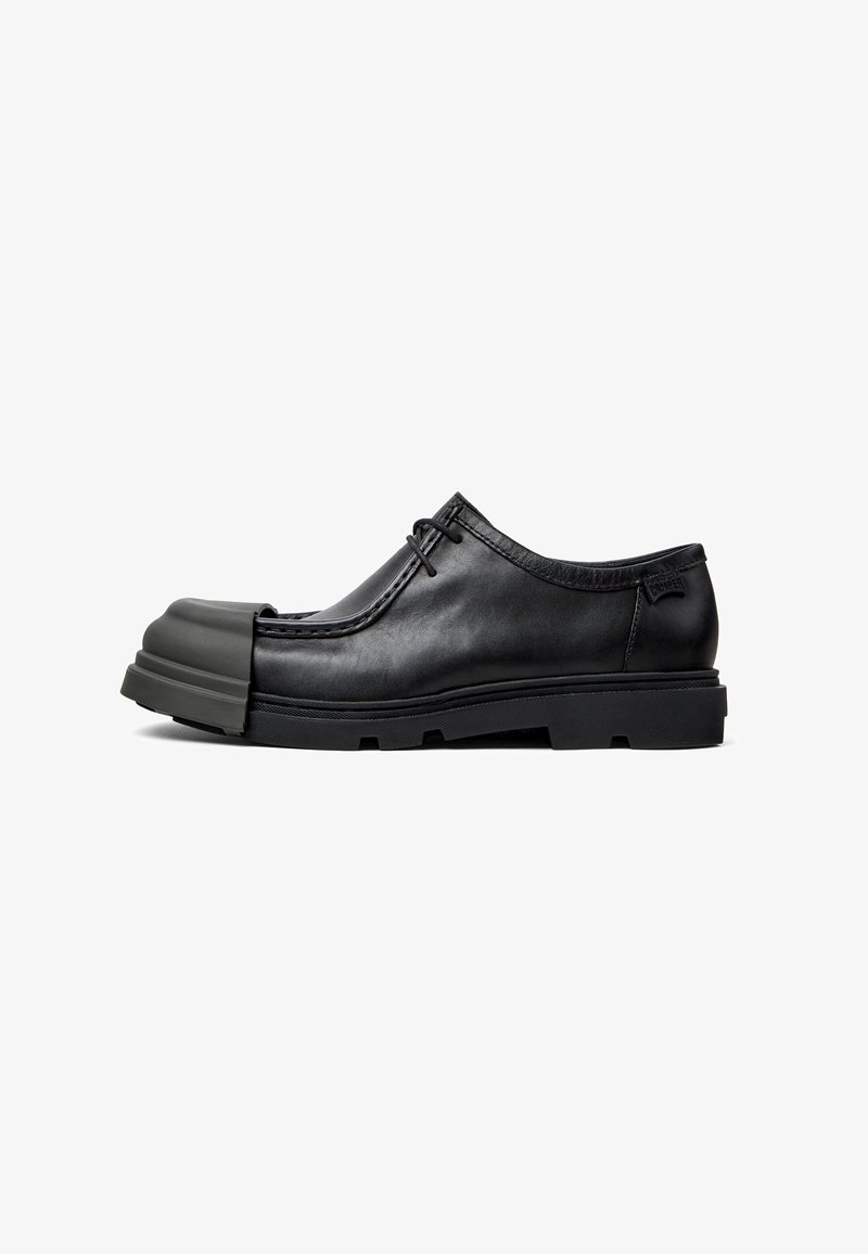 Chaussure noire en cuir avec un bout arrondi distinct, surface texturée, design à lacets et semelle en caoutchouc épaisse.