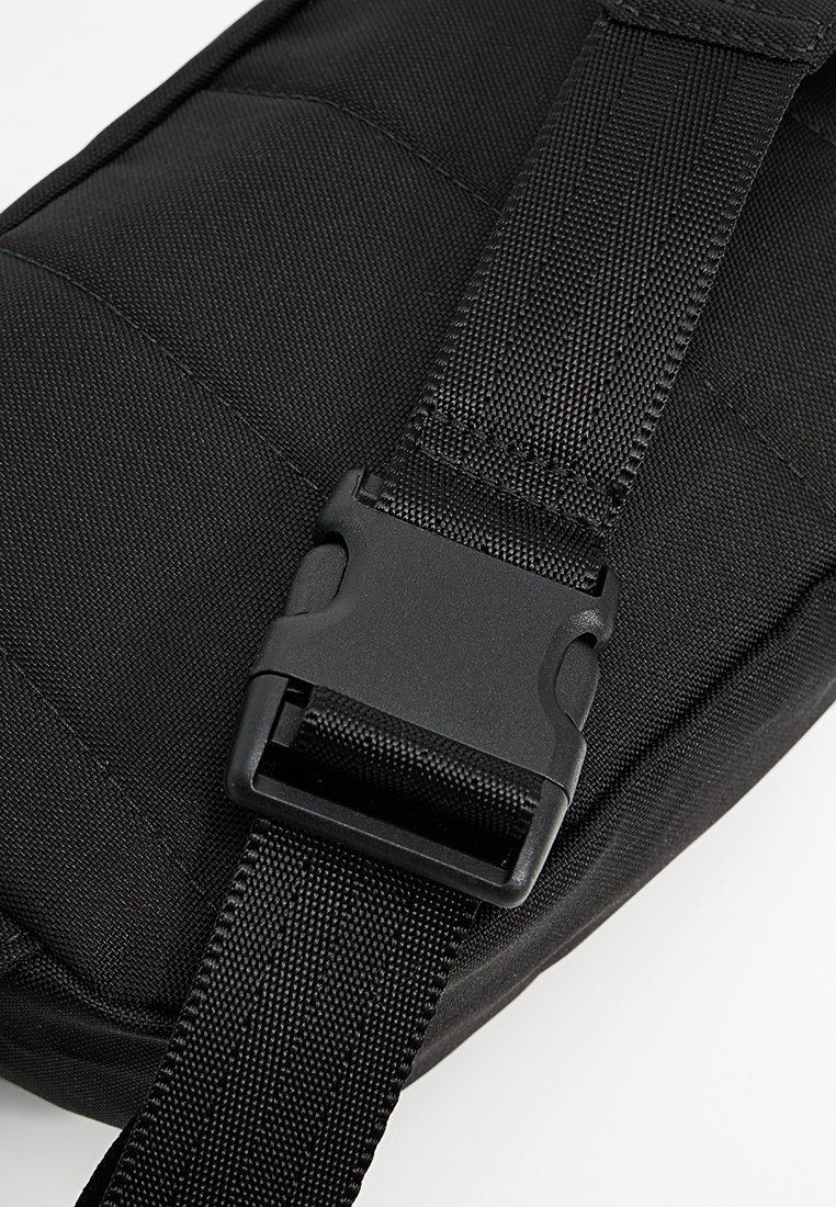 Czarna nylonowa taśma z plastikowym zapięciem na boku przymocowana do wykończonej poduszką powierzchni tekstylnej.