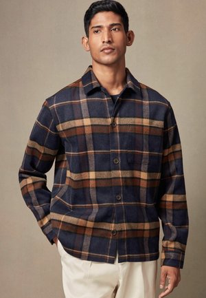 Navy and tan plaid shirt in a soft, textured fabric. Features a collar, button closure, and pocket. Loose fit with long sleeves.