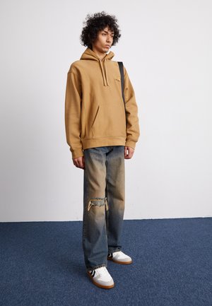 Ruskohvi huppari, millel on esitasku, koos heledate pleekinud siniste teksadega, millel on rebend. Kaetakse valgete spordijalatsitega ja mustade aktsentidega.