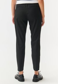 Black tailored pants with a slim fit, featuring a smooth texture and subtle back pockets, paired with black lace-up shoes.