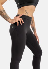 Sorte leggings med en glatt tekstur og høy midje, med en liten logodetalj på siden og forsterkede sømmer for økt holdbarhet.