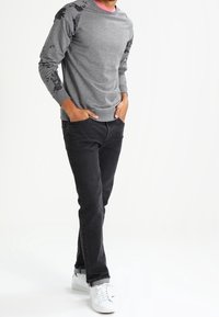 Sudadera gris con mangas de patrón oscuro, combinada con jeans negros y zapatillas blancas. El diseño es casual y estructurado.