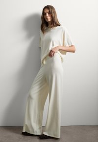 Ensemble t-shirt oversized crème et pantalon large, fabriqué à partir d'un tissu doux, présentant une texture subtile et une coupe décontractée avec un cordon de serrage réglable.
