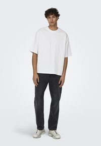 Witte katoenen t-shirt met een losse pasvorm, gecombineerd met donkere jeans en witte sportieve schoenen. Eenvoudig design, korte mouwen, ronde hals.