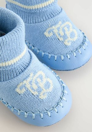 Helleblaue Babyschuhe mit gestrickten Oberteilen, einem gerippten Bündchen und weißer Schrift. Die Sohle weist genähte Akzente und eine glatte Textur auf.