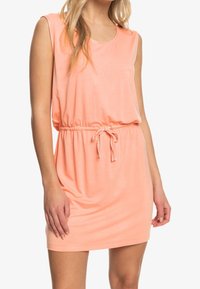 Robe sans manches de couleur pêche avec une coupe décontractée, taille à cordon et tissu léger et doux. Texture lisse sans motifs ni accents.