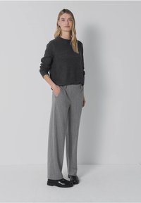 Pull en maille gris associé à un pantalon large à rayures fines gris clair et des chaussures noires. Design simple avec une coupe décontractée et une texture douce.