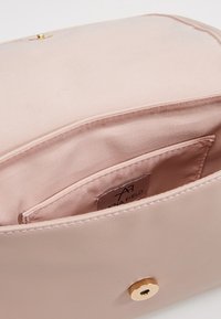 Różowe wnętrze syntetycznej torebki z pojedynczą kieszenią i metką, charakteryzujące się gładką teksturą oraz złotym zapięciem na zatrzask.