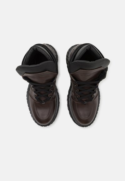 Brązowe skórzane sneakersy za kostkę z czarnym wyściełanym kołnierzem, okrągłym noskiem, solidną gumową podeszwą i czarnymi sznurówkami. Gładka faktura i minimalne detale.