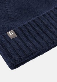 Mörkblå stickad mössa med ribbat mönster. Har en liten rektangulär logotypatch med bokstaven "B" på sidan.