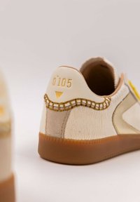 Sneaker beige con pelliccia testurizzata e dettagli in pelle liscia, caratterizzata da accenti gialli, un bordo cucito e il numero stampato "0105" sul tallone.
