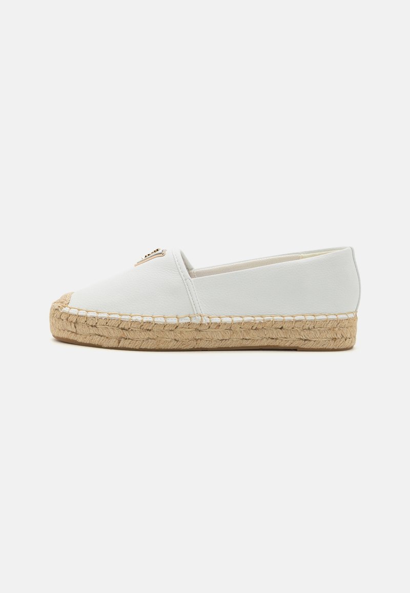 Espadrille blanche à enfiler avec semelle en jute tissée et petit emblème métallique sur le dessus, vue de côté sur fond uni.