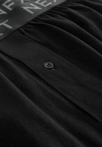 Schwarzes Kleid mit einem gerafften Design, Knopfverschluss und strukturiertem Taillenband, beschriftet mit hellgrauer Schrift.