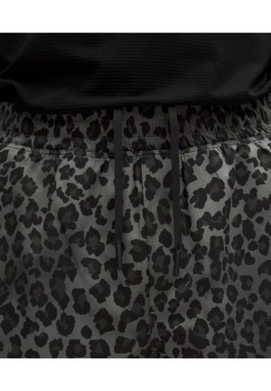 Pantalon gris avec motif léopard noir et cordons noirs à la taille élastique, porté avec un haut noir.