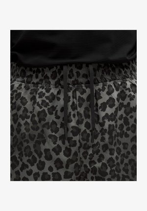 Pantalon gris avec motif léopard noir et cordons noirs à la taille élastique, porté avec un haut noir.