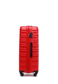 Valise rigide rouge avec texture striée, fermeture éclair et serrure noirs, poignée télescopique et quatre roues pour une mobilité aisée.