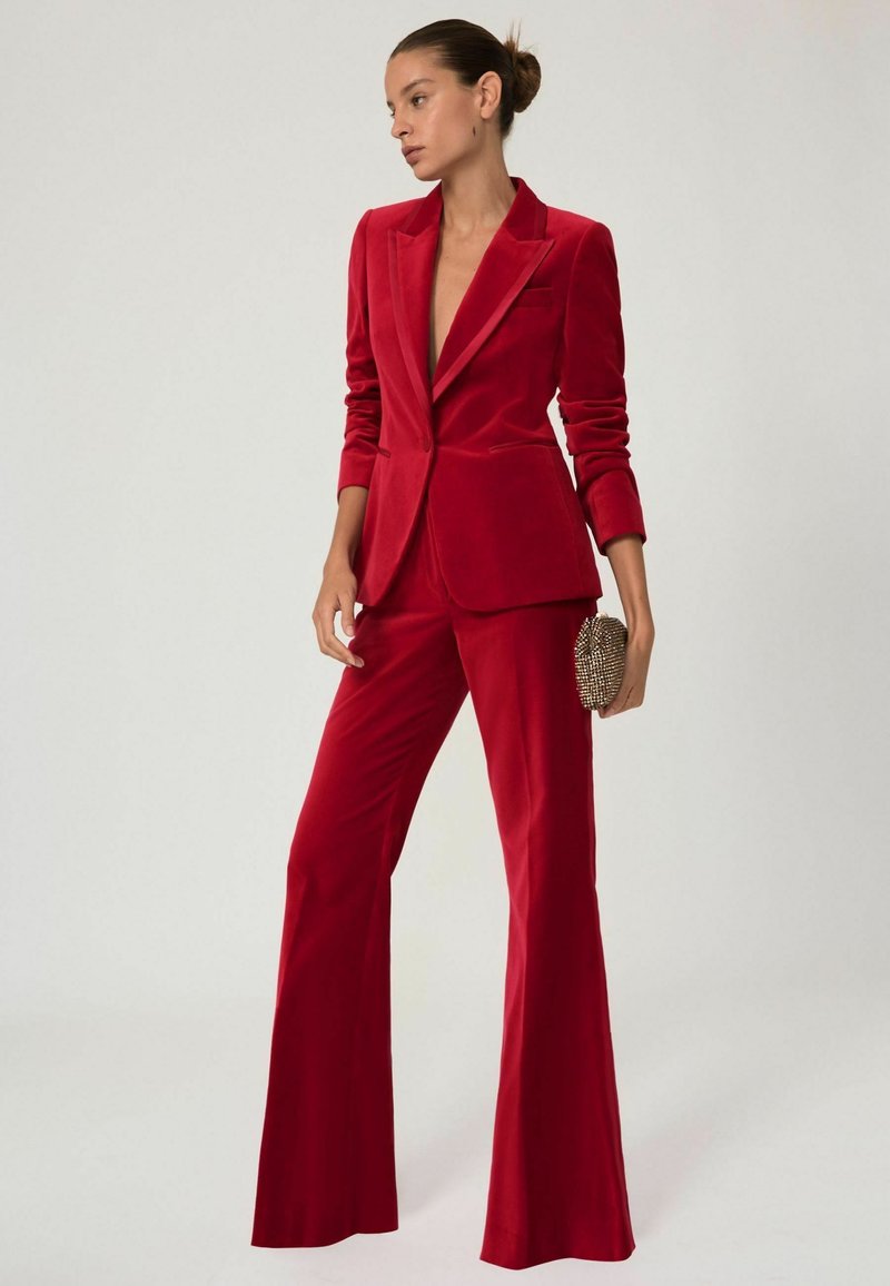 Rød fløjlssæt med en tætsiddende blazer og udsvingede bukser, med en dyb udskæring og en tekstureret, prydet clutch.