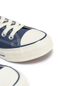 Tumesinine kanvas sneakers kreemja kummist varbakee ja tallaga, valged paelad ja hõbedased silmad. Omab tekstuuriga tallat, mis tagab haarde ja vastupidavuse.