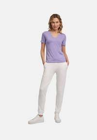 T-shirt lilac a scollo a V con maniche corte, abbinato a pantaloni della tuta bianchi a gamba affusolata e sneaker bianche. Realizzato in cotone misto, design casual.