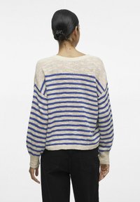 Pull-over rayé beige et bleu, avec une coupe ample, des épaules basses et des poignets côtelés. Matière tricotée texturée et longueur cropped.