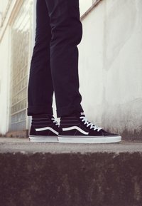 Czarne sneakersy za kostkę z zamszu z białymi akcentami, z kontrastującymi szwami i białymi sznurówkami, w zestawieniu z ciemnymi spodniami.