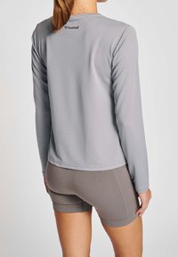 Graues langärmliges Sportoberteil mit Rundhalsausschnitt und strukturiertem Stoff, mit dem Hummel-Logo auf der oberen Rückseite. Kombiniert mit grauen Shorts.