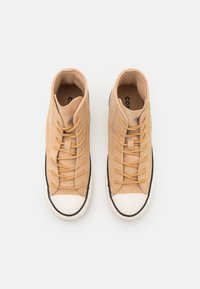 Zapatillas altas de ante beige claro con cordones amarillos y puntera de goma blanca. Detalles en negro a lo largo de la suela. Diseño clásico.