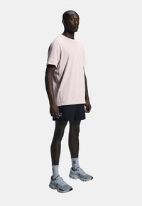 Lyserød kortærmet skjorte med et logo, parret med sorte shorts. Båret med hvide sokker og grå sneakers med sorte detaljer.