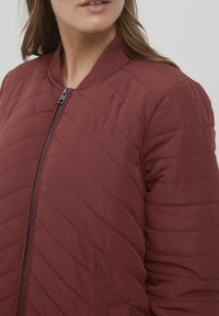 Röd vadderad jacka med zip-framdel, ribbad krage och diagonalt sydda mönster. Mjuk textur, lätt vikt och figursydd silhuett.