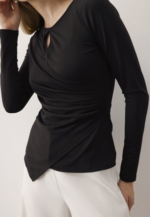 Top nero a maniche lunghe con scollatura a chiave, dettagli arricciati e vestibilità tailored. Realizzato in tessuto morbido ed elasticizzato.