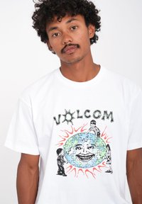 Witte katoenen T-shirt met een kleurrijke grafische print van cartoonfiguren, zonnestraal-accenten en het woord "VOLCOM" in gestileerde letters.