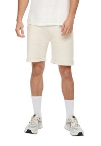 Beige Baumwollshorts mit aufgerollten Säumen, kombiniert mit weißen Socken und hellen Sportschuhen mit grauen Akzenten.