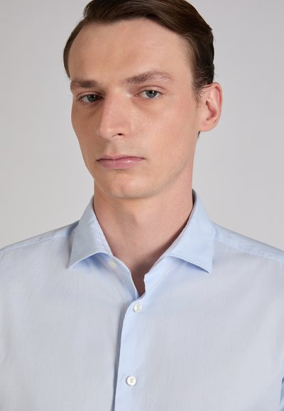 Camisa azul claro abotonada con una textura suave, que presenta un cuello clásico, un diseño de corte recto y una tapeta frontal estándar con botones.