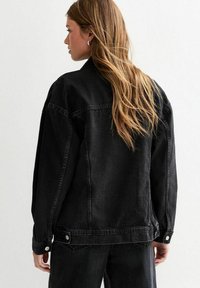 Veste en denim noir au fit décontracté, avec des coutures visibles, des accents de boutons et des poches à rabat, présentant une texture légère et un design structuré.