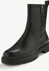 Bottine en cuir noir avec fermeture éclair latérale, bout arrondi, semelle épaisse en caoutchouc et languette à l'arrière.