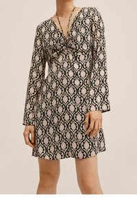 Mekko musta- ja kermavärisellä kuviolla, pitkät hihat, V-pääntie ja solkieurastus rinnassa. Sisältää kukkamotiiveja vaaleanpunaisen ja beigen sävyissä.