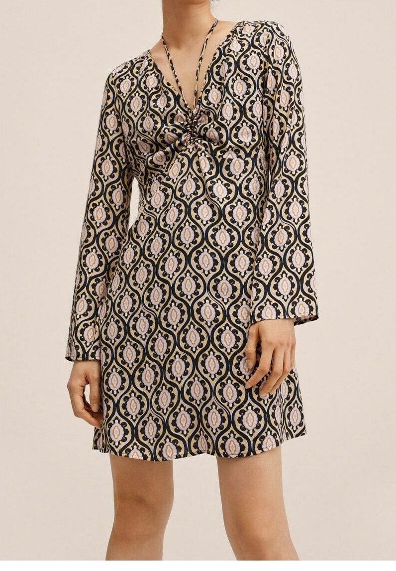 Mekko musta- ja kermavärisellä kuviolla, pitkät hihat, V-pääntie ja solkieurastus rinnassa. Sisältää kukkamotiiveja vaaleanpunaisen ja beigen sävyissä.