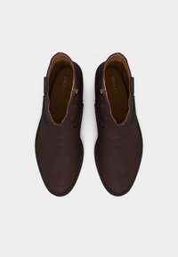 Ζευγάρι σκουρόκαφέ δερμάτινων μποτών αστραγάλου με πλευρικά φερμουάρ, σε θέα από πάνω πάνω σε απλό ανοιχτό υπόβαθρο.