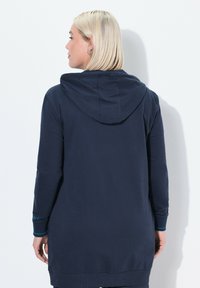 Abito felpa blu navy con cappuccio, maniche lunghe e polsini a costine. Presenta una texture uniforme e accenti blu a contrasto sui polsini.