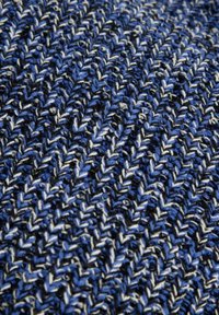 Tessuto in maglia con un motivo a spina di pesce blu, nero e bianco, che presenta una superficie texture con spessori di filato variabili.