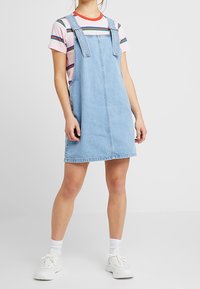 Jeansklänning med justerbara axelremmar, ljusblå färg, rak skärning, bärs över en randig t-shirt, matchad med vita sneakers.