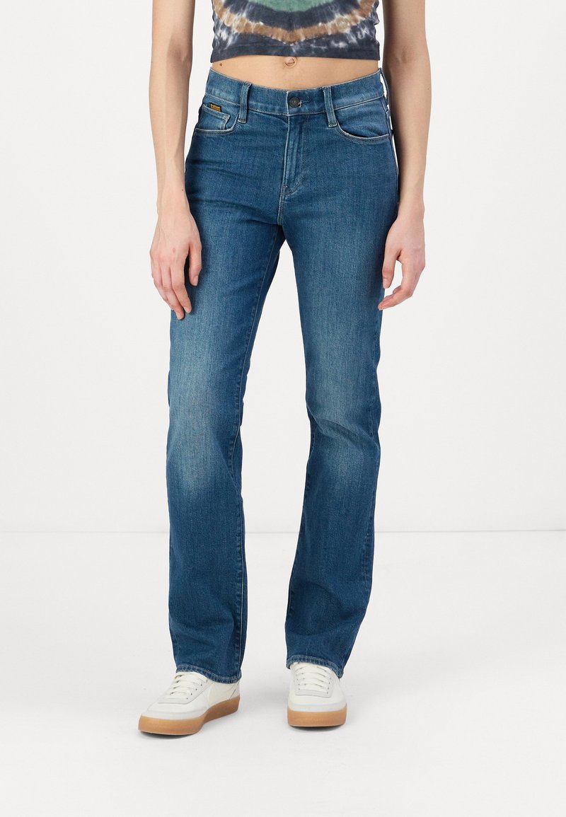 Vaqueros de denim azul con un ajuste recto, cintura media y bolsillos frontales. Llevados con zapatillas blancas.