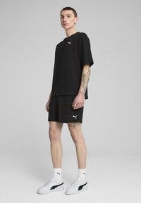 T-shirt noir à manches courtes avec un logo blanc, associé à un short noir avec des poches latérales. Porté avec des baskets blanches et des chaussettes côtelées.