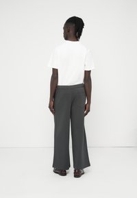 Χαλαρά γκρι παντελόνια με υφή υφάσματος, ελαστική μέση και πίσω τσέπη, συνδυασμένα με ένα απλό λευκό κοντομάνικο πουκάμισο.