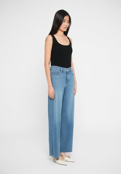 Sort tætsiddende top med en rund halsudskæring, kombineret med brede lyseblå denim jeans. Modellen bærer brune spidse sko med en lav hæl.